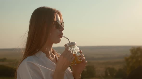 Woman in White Shirt and Sunglasses Drinks Cocktail and Smiles