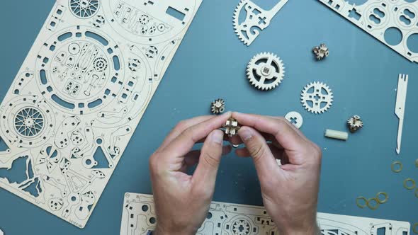 Man holding little flywheel gear detail in hands, assembling mechanical wooden puzzle toy