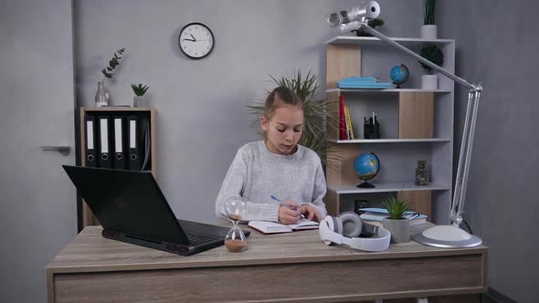  Teen Girl with Long Light Hair Sitting at Her Home Workplace and Working with Computer and Notebook