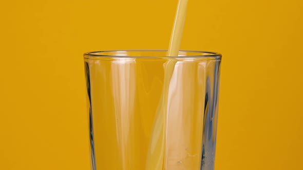 Pouring fresh orange juice in drinking glass over yellow background