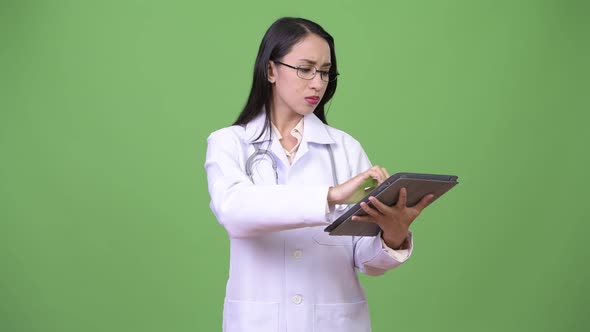 Young Beautiful Asian Woman Doctor Thinking While Holding Digital Tablet