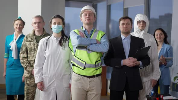 Portrait of Confident Caucasian Builder in Vest and Hart Hat Crossing Hands Looking at Camera with