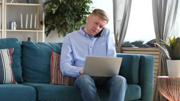 Middle Aged Man Talking on Phone and Working on Laptop