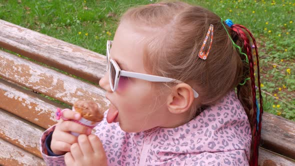 Pretty little girl eating an ice cream in waffle cone on bench outdoor Child bites chocolate gelato