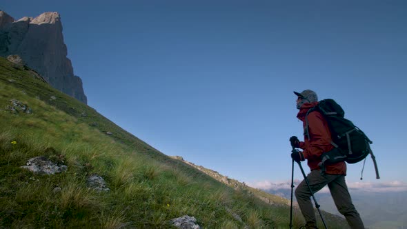 Young Caucasian Woman Tourist with a Backpack and Trekking Poles in Caps and Sunglasses on a Summer