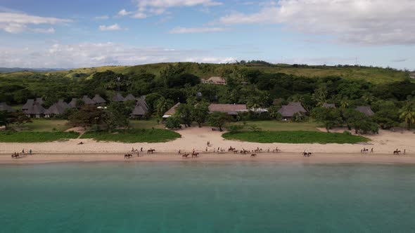 Static drone watching people riding horses along the Natadola beach in Fiji with Yatule Resort and s