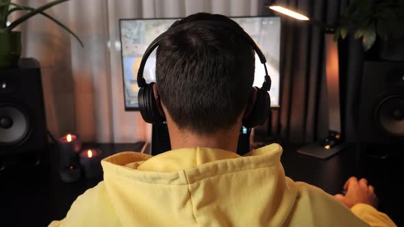 Back view of male gamer guy wearing headphones playing action shooter video game