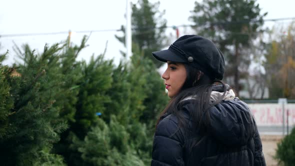 A hispanic woman shopping for a seasonal holiday Christmas tree decoration on a lot with many specie