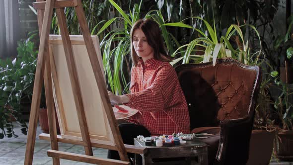 Artist in an Art Studio with Plants Young Pretty Woman Drawing a Painting with Colors and Looking