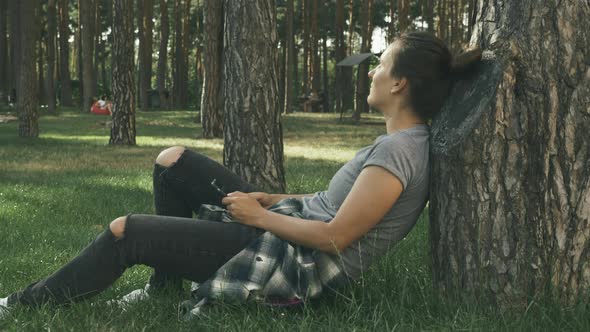 Portrait of young brunette woman relaxing with skateboard in park at sunset.