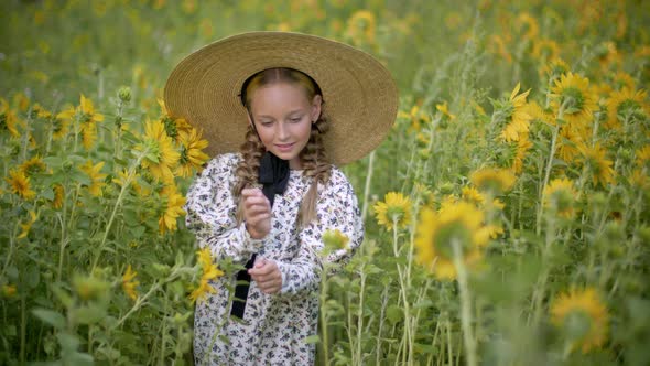 Romantic Girl with Two Braids and Straw Hat Walking on Blooming Sunflowers Meadow. Rustic Girl in