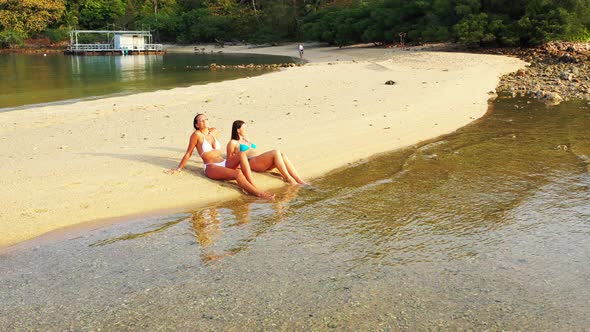 Modern smiling girls travelling in the sun at the beach on clean white sand and blue background 