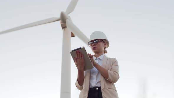 An Engineer Girl in a Jacket and Hard Hat Holds a Digital Tablet and Looks Into the Distance