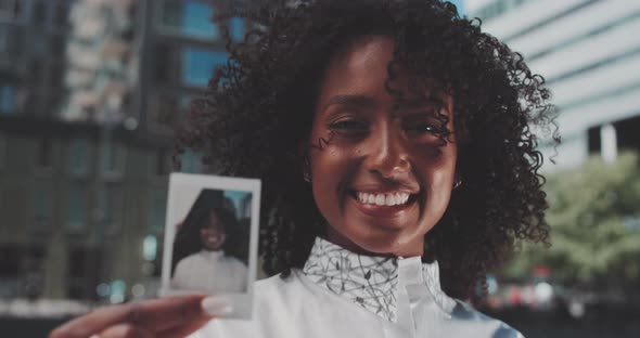 Attractive african woman smiling and showing a instant photo of herself  to the camera