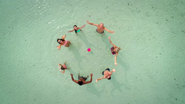 Aerial view of group of friends in swimwear playing volleyball in sea near beach.