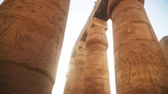 Massive pillars with intricate carved images and hieroglyphs in the Kamak Temple, Luxor, Egypt. Sun