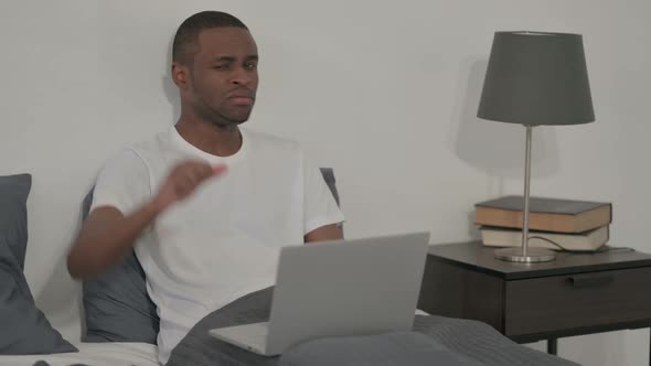 African Man Showing Thumbs Down Sign While Using Laptop in Bed
