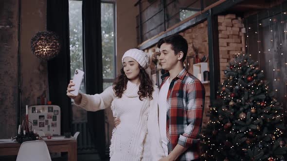 Young Couple Dressed in Christmas Clothes, Having Fun and Taking Pictures with Their Phone Near the