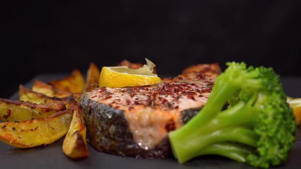 Roasting salmon fillets rotating on a black background with lemon slice, french fries