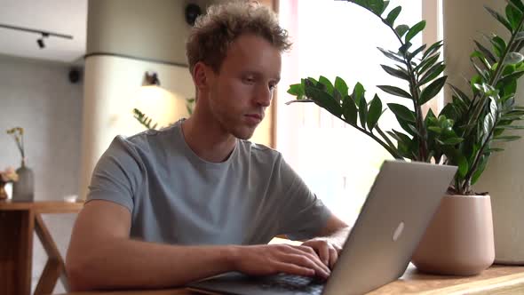 Attractive guy sitting at the table and working on a laptop