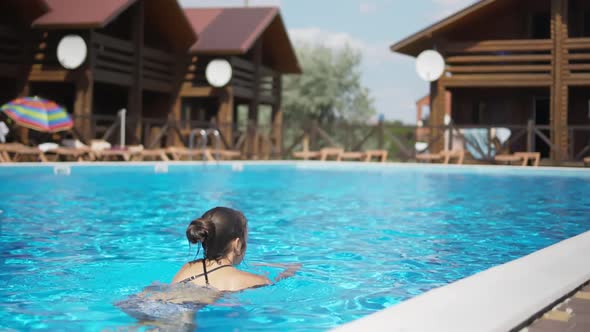 Girl in a Leopard Swimsuit Swims in a Pool with Blue Water on a Summer Day