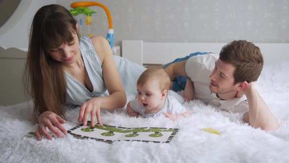 Young Parents Reading Book To Thier Baby Daughter Lying on a Bed