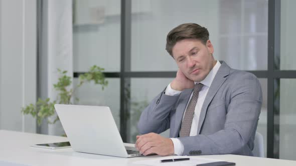 Middle Aged Man having Neck Pain while using Laptop in Office