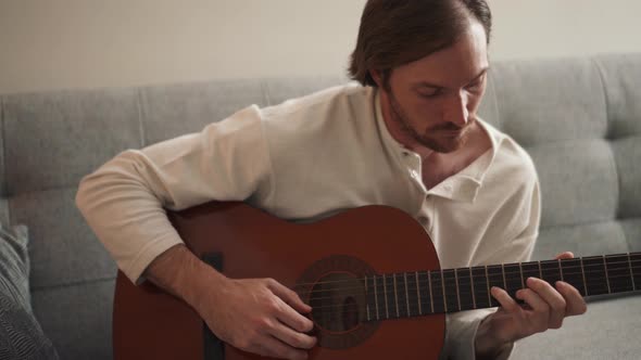 Serious long-haired man learns to play the guitar from a video lesson