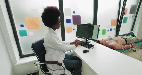 African American Doctor Is Sitting At A Work Computer That Is Connected To A