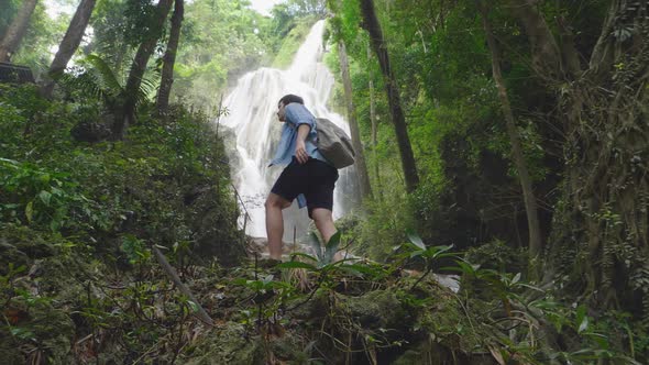 Young Man Walking Towards A Waterfall In Forest