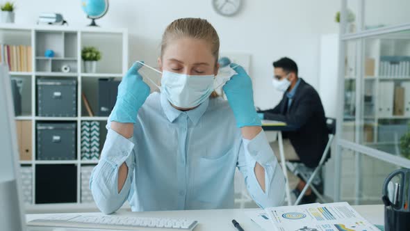 Portrait of Young Businesswoman Taking Off Face Mask and Breathing at Desk in Office