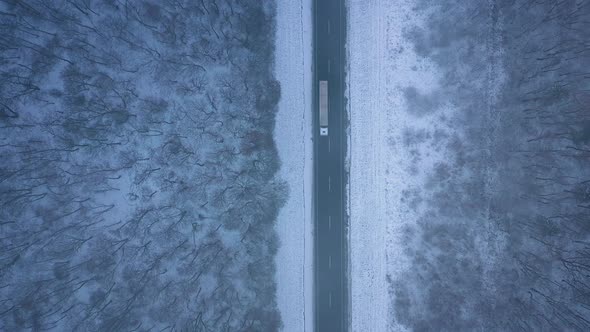 Aerial View of Trucks on the Road Passing Through the Winter Forest in Blizzard