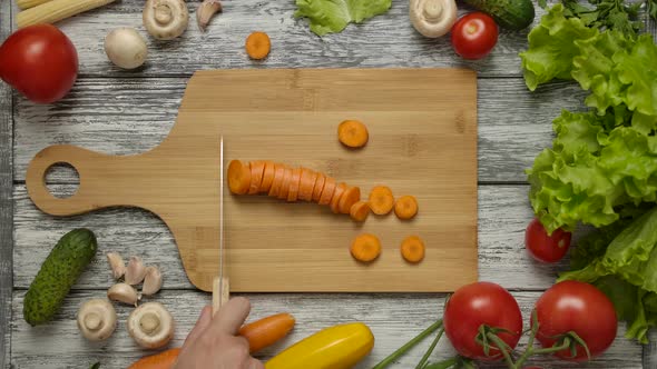 Cook Moving Sliced Carrot with Knife on Cutting Board.