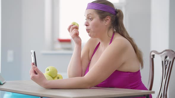 Side View of Plussize Caucasian Young Woman Eating Healthful Organic Vitamin Apple Looking at