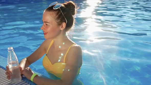 Young Woman in a Swimsuit Drinks Cool Water From a Plastic Bottle in the Pool