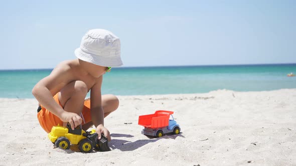 Happy Kid Playing with Cars on the Beach on the Horizon Azure Sea and Blue Sky