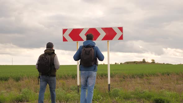 Travelers with Backpacks Come To the Road Sign at the Intersection and Choose Their Route. Teamwork