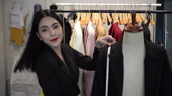 Happy Smiling Asian Female Tailoring Fashion Designer with Mannequin and Suit Jackets on Hanger