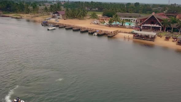 Cinematic drone shot of Aqua Safari Resort lake side in Ghana, West Africa, showing jetski and boat