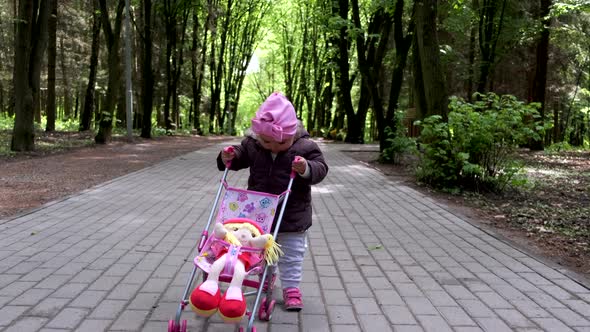 Baby girl walking with her stroller toy in spring park.