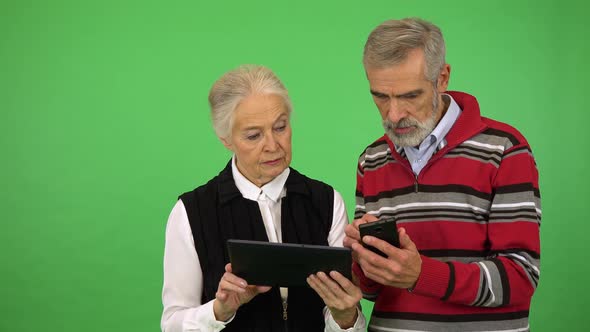 An Elderly Couple Works on a Smartphone and a Tablet - Green Screen Studio