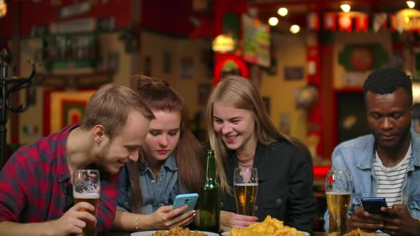 A Man and Two Girls are Sitting in a Bar and Looking at the Phone Screen While in the Company of
