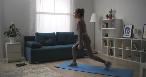 Pretty Young Woman with Ponytail Is Squatting with Dumbbells at Home Exercises for Keeping Fit 