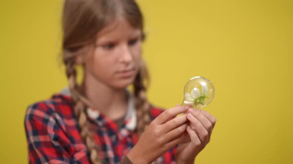 Teenage Blurred Girl Examining White Flower in Light Bulb at Yellow Background