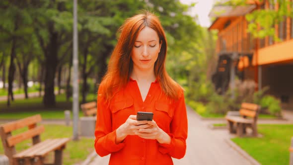 Redhead Woman Scrolls Touch Screen on Smartphone Outdoor