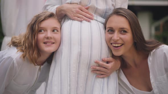 Pregnant Belly of Unrecognizable Woman with Excited Young Lady and Teenage Girl Listening Smiling