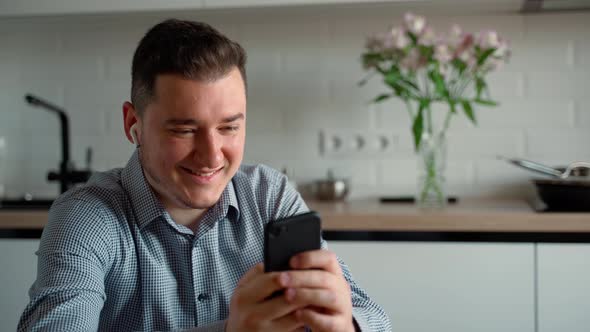 A positive caucasian 30s man playing smartphone telephone sitting at desk