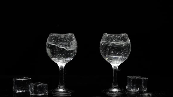 Add Ice Cubes To Shots of Vodka in Glasses. Black Background. Alcohol Drink