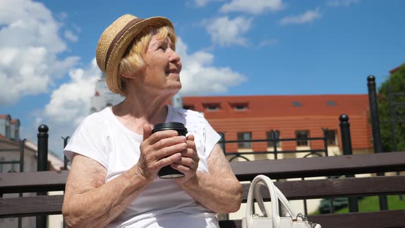 Elderly Woman Resting Outdoors In City With Coffee To Go