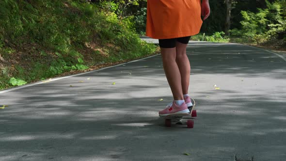 Young Sporty Woman is Skateboarding at Summer Standing on Board and Rolling Over Road